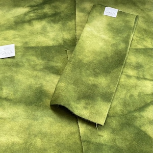 May include: Several pieces of green fabric with a mottled, watercolor-like pattern. The fabric has a soft, textured appearance. Small white tags with text are attached to some pieces.