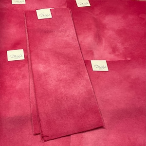 May include: A collection of vibrant pink fabric pieces, varying in size, are arranged together. Each piece has a soft, textured appearance. Small white tags with the text "Stella Wade" are attached to some of the fabric pieces.