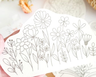 May include: A white sticker with a silver outline of a floral design. The design features a variety of flowers and leaves, including daisies, roses, and ferns.