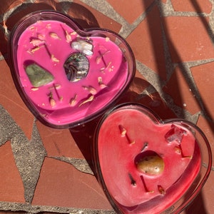 Può includere: Due portacandele di vetro a forma di cuore con candele rosa e rosse. Le candele hanno vari cristalli e fiori secchi incorporati.