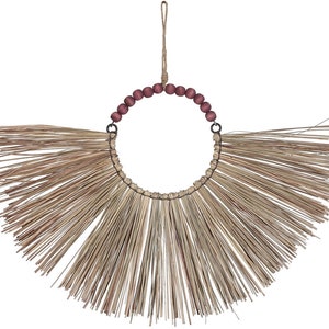 May include: A circular wall hanging with a fan-shaped design made from natural straw. The circle is decorated with dark red wooden beads and a jute loop for hanging. This decorative piece has a bohemian style and would suit any home.