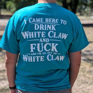 May include: Teal t-shirt with white text that reads "I CAME HERE TO DRINK WHITE CLAW AND FUCK AND I'M ALL OUT OF WHITE CLAW." The shirt is short-sleeved.