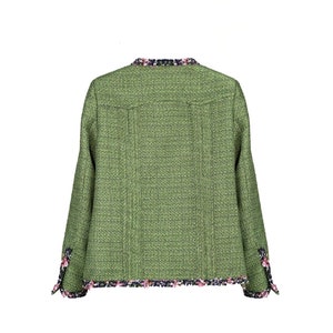 Op de afbeelding: Een groen tweed jasje met een zwarte en roze bies. Het jasje heeft een kraag en lange mouwen.