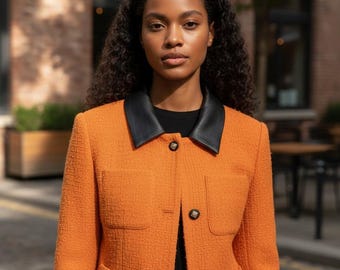 Könnte beinhalten: Eine orangefarbene Tweedjacke mit schwarzem Lederkragen und schwarzen Knöpfen. Die Jacke hat zwei Vordertaschen und wird über einem schwarzen Oberteil getragen. Die Jacke ist ein klassischer Stil.