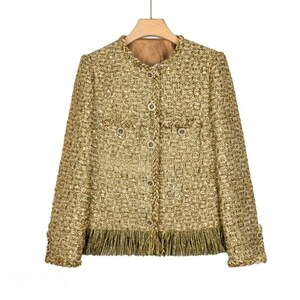 Puede incluir: Una chaqueta de tweed dorada con ribete de flecos y cierre de botones. La chaqueta tiene dos bolsillos en la parte delantera.