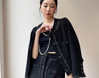 May include: A black tweed jacket and matching skirt set. The jacket has a button-down front and silver trim. The skirt is a mini skirt with matching buttons. A black top and pearl necklace complete the outfit.