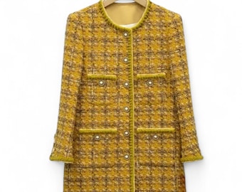 May include: A yellow and brown tweed jacket with a round neckline, long sleeves, and a button closure. The jacket has two pockets on the front and a pearl-like button detail.