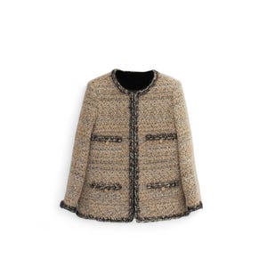 May include: A beige tweed jacket with black trim and gold buttons. The jacket has a round neckline and long sleeves.