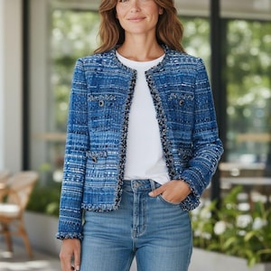 Può includere: Giacca in tweed blu con scollo tondo e bordi sfilacciati. La giacca ha un aspetto strutturato con un mix di fili blu e bianchi. La modella indossa una maglietta bianca e jeans blu. La giacca ha due tasche anteriori e bottoni decorativi.