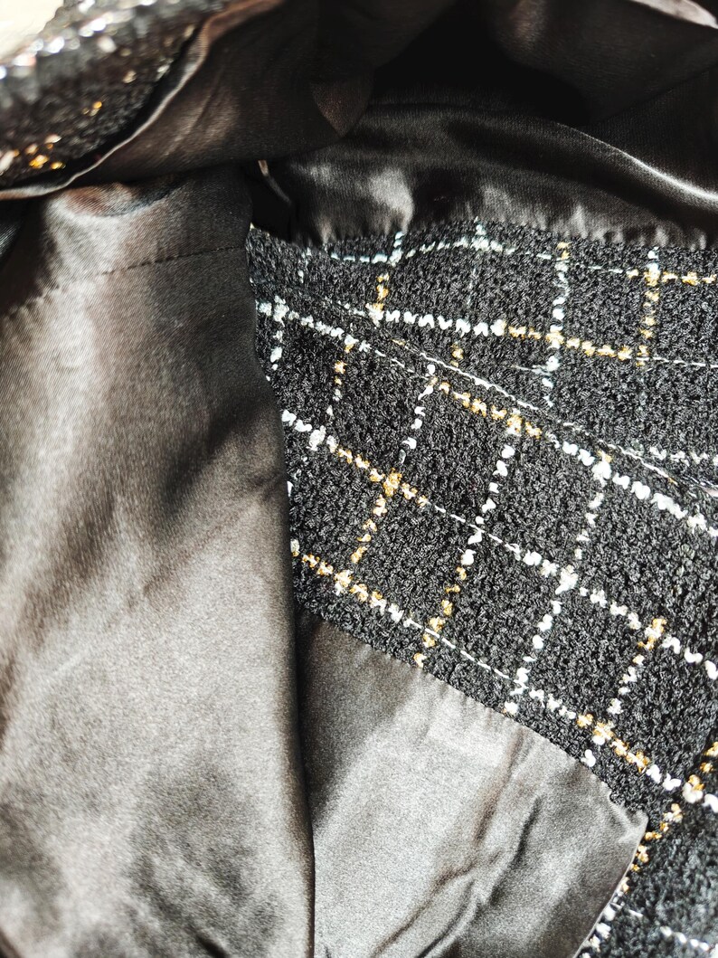May include: Close-up of the inside of a black and white tweed handbag with a black satin lining.