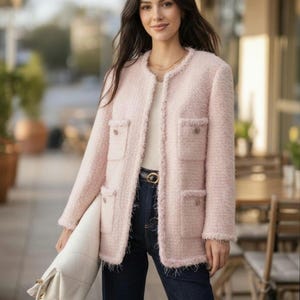 Puede incluir: Chaqueta de tweed rosa claro con cuatro bolsillos delanteros y bordes deshilachados. La chaqueta se lleva con vaqueros azul oscuro y un bolso blanco. El conjunto se completa con un cinturón dorado y una camiseta blanca.