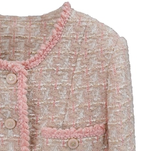 K&ouml;nnte beinhalten: Nahaufnahme einer rosa-beigen Tweedjacke. Die Jacke hat einen runden Ausschnitt, dekorative Kn&ouml;pfe und rosa Bes&auml;tze. Der Stoff hat eine gewebte Textur mit dezenten Goldf&auml;den.