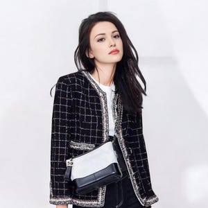 May include: A woman wearing a black and white tweed jacket with a black and white quilted shoulder bag. She is also wearing black jeans and a white t-shirt.