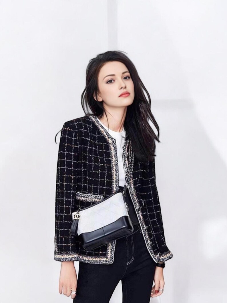 May include: A woman wearing a black and white tweed jacket with a black and white quilted shoulder bag. She is also wearing black jeans and a white t-shirt.