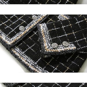 May include: Black and white tweed fabric with a gold thread woven into the pattern. The fabric has a white and beige trim around the edges.