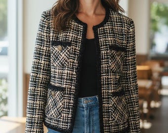 Könnte beinhalten: Eine schwarz-weiß-beige Tweedjacke mit rundem Ausschnitt und Vordertaschen. Die Jacke hat goldene Knöpfe und schwarze Paspeln. Die Person trägt eine blaue Jeans und ein schwarzes Oberteil.