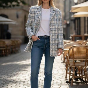 Op de afbeelding: Een vrouw draagt een lichtblauwe en witte geruite blazer, een wit t-shirt en een blauwe jeans. Ze draagt witte sneakers. De outfit is geschikt voor een casual, alledaagse look.