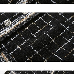May include: Black and white tweed fabric with a subtle gold thread woven in. The fabric has a textured surface and is trimmed with a black and white fringe. There are silver buttons on the fabric.
