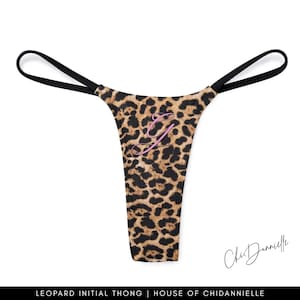 Könnte beinhalten: Leopardenmuster-Tanga mit schwarzen Trägern und einem rosa Initial "G". Der Tanga hat ein braunes und schwarzes Fleckenmuster. Der Text "ChiDannielle" befindet sich unten rechts.