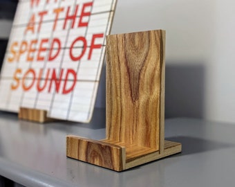 Peut inclure: Un support en bois avec une finition grain de bois naturel. Le support est conçu pour tenir un petit objet, comme un livre ou un cadre photo. Le support est composé de deux morceaux de bois assemblés à angle droit.