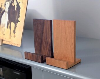May include: Two wooden stands for displaying items, one crafted from dark brown walnut wood and the other from a lighter, reddish-toned wood. Each stand features a vertical back panel and a horizontal base ledge to support objects upright.