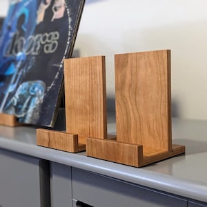 May include: Three wooden record album display stands. The stands are made of light brown wood with a natural wood grain finish. The stands are stacked on top of each other, with the largest stand on the bottom and the smallest stand on top.