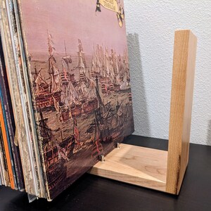 May include: A wooden record stand with a natural finish, holding a vinyl record with a painting of a naval battle. The record is titled "The Battle of Trafalgar".