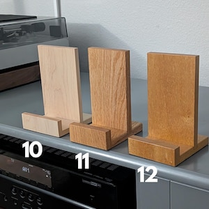 Handcrafted wooden now playing stand displayed as 3 separate stands siting on a gray tabletop. Featuring maple, oak, and movingui. Numbered 10-12