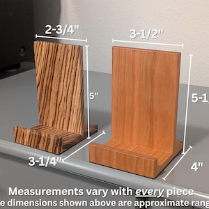 Two wooden record display stands shown side by side on a gray surface, one made of zebrawood and the other of cherry wood. White measurement lines indicate approximate dimensions: the zebrawood stand measures about 5 inches tall, 3-1/4 inches deep, and 2-3/4 inches wide, while the cherry stand measures about 5-1/4 inches tall, 4 inches deep, and 3-1/2 inches wide. Text below notes that measurements vary with every handmade piece.