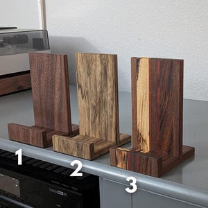 Handcrafted wooden now playing stand displayed as 3 separate stands sitting on a gray tabletop. Featuring walnut, black limba. and walnut/hackberry Numbered 1-3