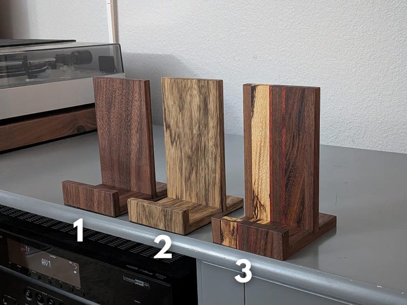 Handcrafted wooden now playing stand displayed as 3 separate stands sitting on a gray tabletop. Featuring walnut, black limba. and walnut/hackberry Numbered 1-3