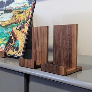 Puede incluir: Cuatro soportes de discos de madera de diferentes tamaños, hechos de madera de nogal oscuro, sobre una superficie gris.