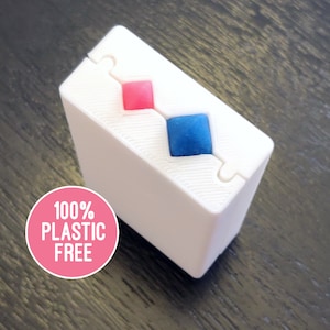 May include: A white, rectangular box with a red and blue diamond shape on the top. The box is made of a material that is 100% plastic free.