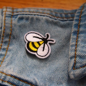 May include: A white and yellow embroidered bee patch on a blue denim jacket.