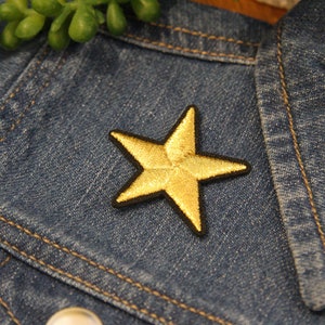 May include: A gold star-shaped patch sewn onto a blue denim jacket.