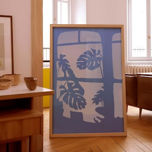 May include: A framed print of a blue silhouette of tropical leaves against a light blue background. The print is in a light wood frame and is leaning against a wall.