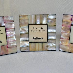 May include: Three square picture frames featuring a mosaic border of iridescent mother-of-pearl tiles. Each frame holds a display card with the text 2 in x 2 in, 5.2 cm x 5.2 cm, and Pier 1 imports. The frames have a glossy, multi-colored finish.