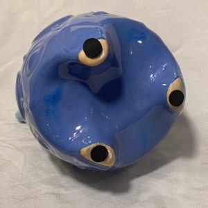 May include: Blue ceramic piggy bank with three black feet and a textured surface.