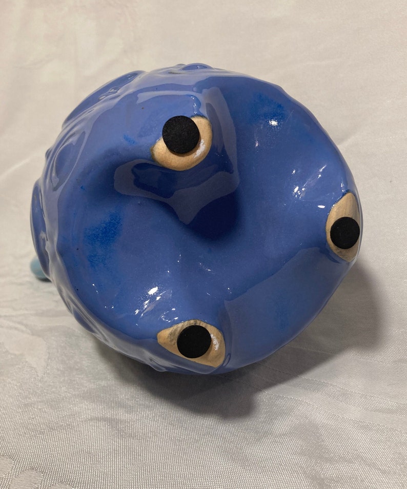 May include: Blue ceramic piggy bank with three black feet and a textured surface.