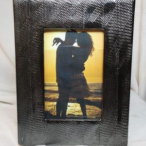 May include: A dark grey rectangular photo frame with a textured finish. The frame contains a picture of a couple silhouetted against a sunset on a beach. The frame appears to be made of a metallic material.