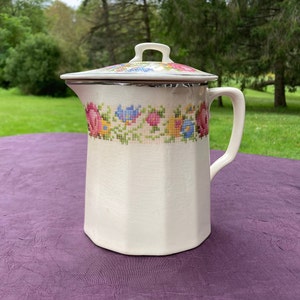 May include: White ceramic pitcher with a floral design and a lid. The pitcher has a handle and a silver trim around the lid.