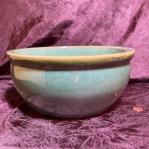 May include: A large, green glazed ceramic bowl with a brown rim. The bowl has a drainage hole in the bottom.