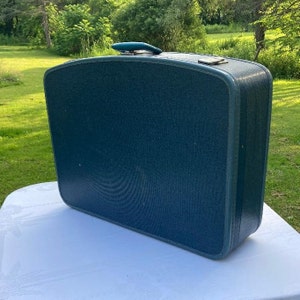 May include: A vintage teal blue suitcase with a metal handle and a textured fabric exterior.
