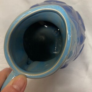 May include: A blue ceramic pitcher with a textured exterior and a smooth, glazed interior. The pitcher has a wide mouth and a handle.