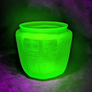 May include: A glowing green glass vase with etched floral and geometric patterns. The vase has a wide, open top and a rounded body. The glass appears to be a vibrant, almost neon, green color, with the etched designs adding texture and detail.
