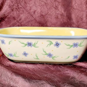 Puede incluir: Fuente de horno rectangular de cerámica crema, interior amarillo y borde azul. El exterior está decorado con motivos florales azules y hojas verdes. La fuente tiene dos asas pequeñas. Adecuada para hornear.