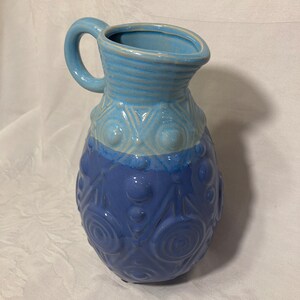 May include: A blue ceramic pitcher with a textured design. The pitcher has a light blue top and a darker blue bottom. The pitcher has a handle and a round body.