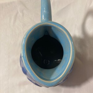 May include: A blue ceramic pitcher with a textured exterior and a light blue glaze. The pitcher has a wide mouth and a handle.