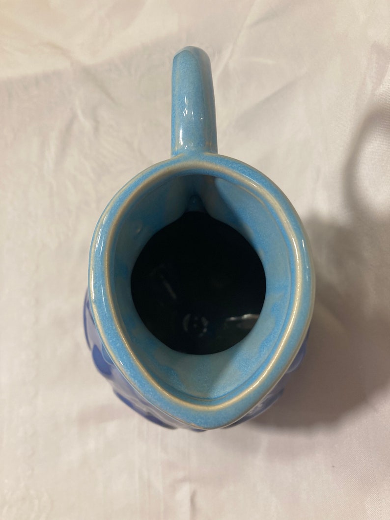 May include: A blue ceramic pitcher with a textured exterior and a light blue glaze. The pitcher has a wide mouth and a handle.