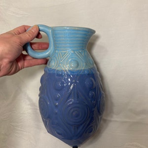 May include: A blue and light blue ceramic pitcher with a textured design. The pitcher has a rounded body and a handle.